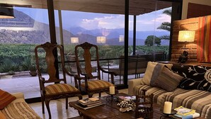 Amplia sala de estar con un gran ventanal corredero que da a un patio, con un sofá, sillas, una mesa de centro y una chimenea.