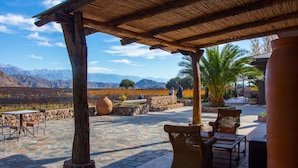 Un patio exterior con piso de piedra, mobiliario de mimbre y vistas a montañas y viñedos.