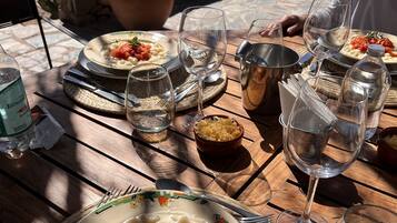 A table set with plates of pasta, glasses, and a bottle of water, with a vineyard view in the background.