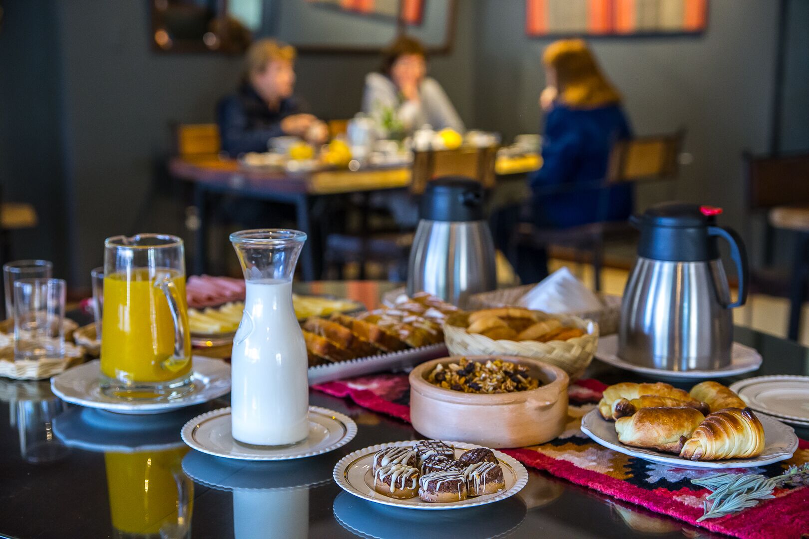 A breakfast table with various pastries, a coffee pot, and a jug of orange juice.
