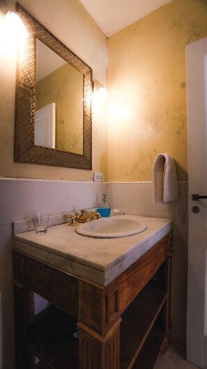 A bathroom with a wooden vanity, a large mirror, a sink with a faucet, and a towel hanging on the wall. - Casa de huéspedes Chañarmuyo (Chañarmuyo)