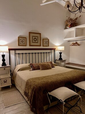 A bedroom with a bed, bedside tables, a bench, and wall-mounted shelves. - Casa de huéspedes Chañarmuyo (Chañarmuyo)
