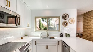 Une cuisine moderne avec des meubles blancs, une cuisinière en acier inoxydable et une fenêtre donnant sur l’extérieur.