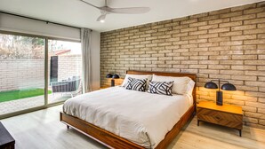 Une chambre avec un mur en briques, un grand lit, un ventilateur de plafond et une table de chevet avec des lampes.