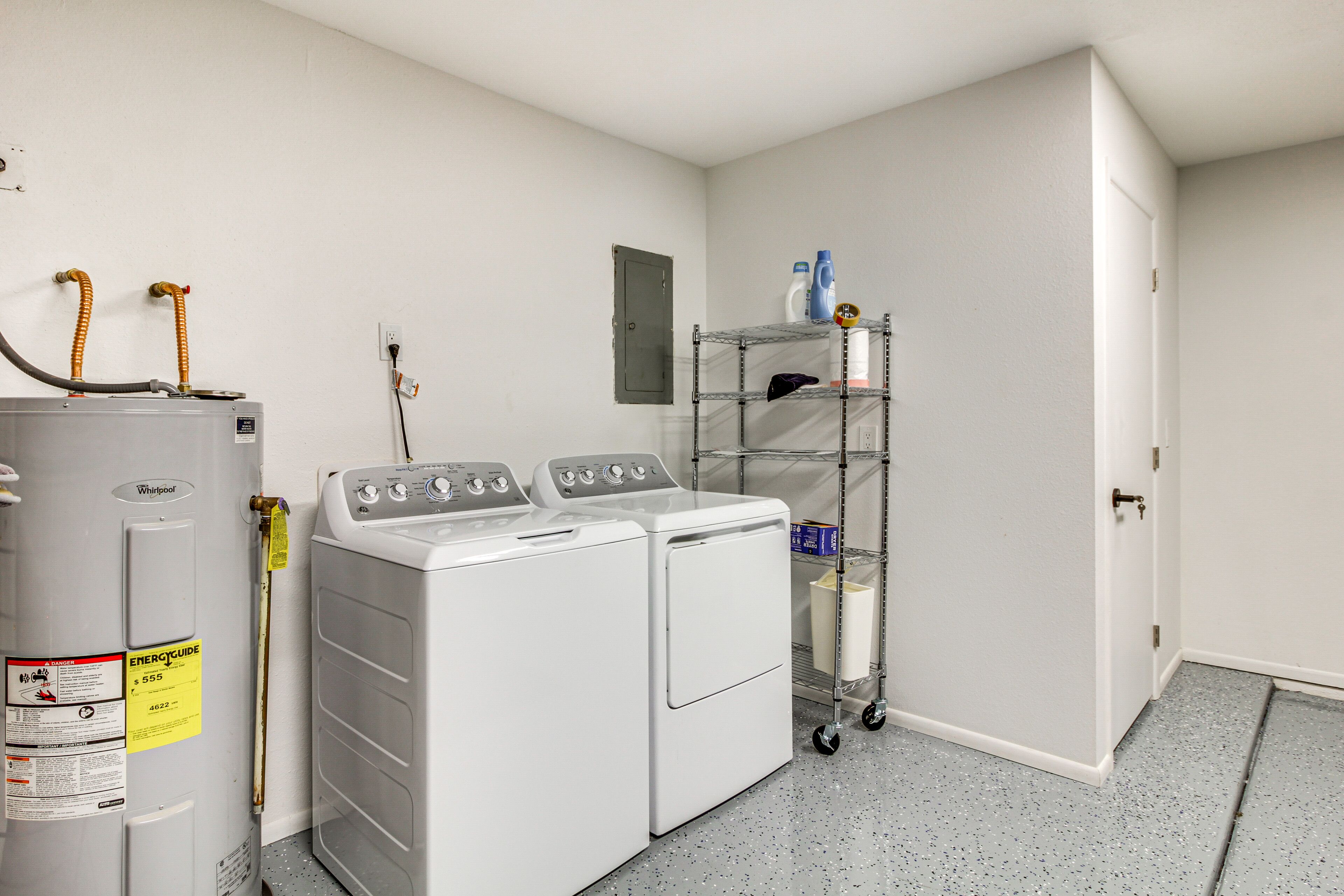 A laundry room with a Whirlpool washer and dryer, a water heater, and a metal shelving unit with cleaning supplies.