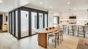 Une cuisine moderne avec des meubles blancs, un four à micro-ondes en acier inoxydable et une table à manger en bois avec quatre chaises.