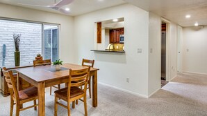 Uma sala de jantar com mesa e cadeiras de madeira, um ventilador de teto e vista através de uma porta de vidro.