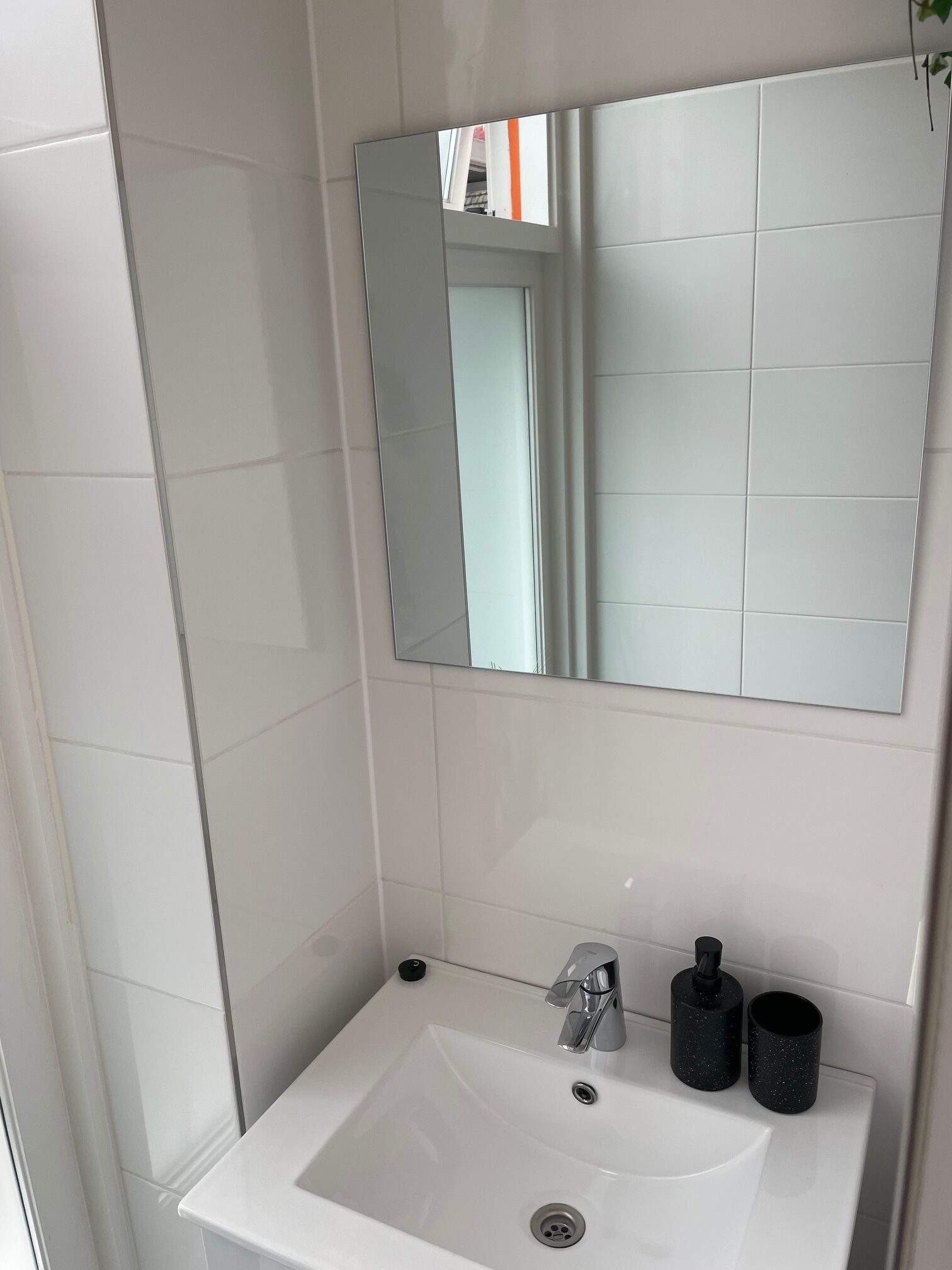 Une salle de bain avec un lavabo blanc, un miroir et deux tasses noires.