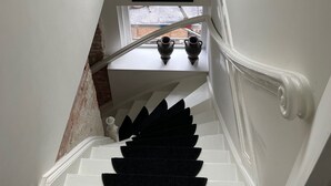 A staircase with a black carpet, a framed picture on the landing, and a window with a view of the street.