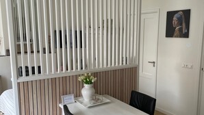 A modern dining area with a white table, black chairs, a white vase with flowers, and a wooden panel wall.
