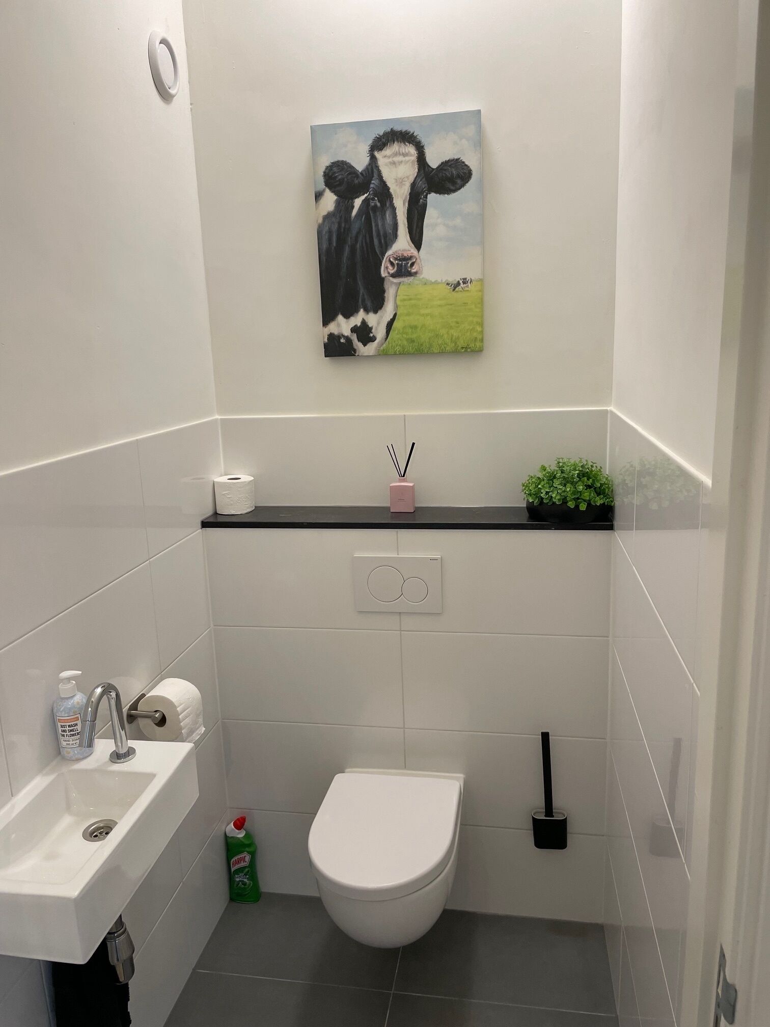 Un baño con inodoro, lavamanos y un cuadro de una vaca en la pared.