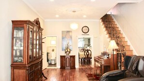 A spacious living room with hardwood flooring, a grand piano, a black leather sofa, and a staircase with ornate railings.