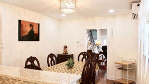 A dining area with a patterned table, wooden chairs, a chandelier, and a staircase leading to another room.
