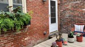 A brick building with a wooden deck, potted plants, and a chair. - Bright & Modern Home with Patio (Philadelphia)