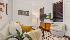 A living room with a sofa, armchair, and a coffee table. There is a TV on a stand, a lamp, and a plant. - Bright & Modern Home with Patio (Philadelphia)