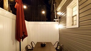 An outdoor patio with a wooden table and chairs, a red jacket hanging on a hook, and string lights.