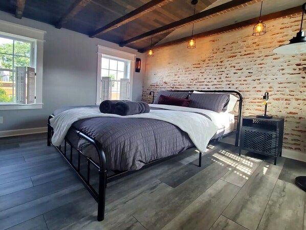 A bed with a metal frame, a bedside table with a lamp, and a brick wall.