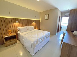 Habitación de hotel con una cama grande, cabecera de madera, dos lámparas de noche, una mesita y una ventana.