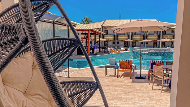 A hanging chair with a cushioned seat and a woven backrest, overlooking a pool area with lounge chairs and umbrellas. - Príncipe do Muta Hotel Design (Santa Cruz Cabralia)