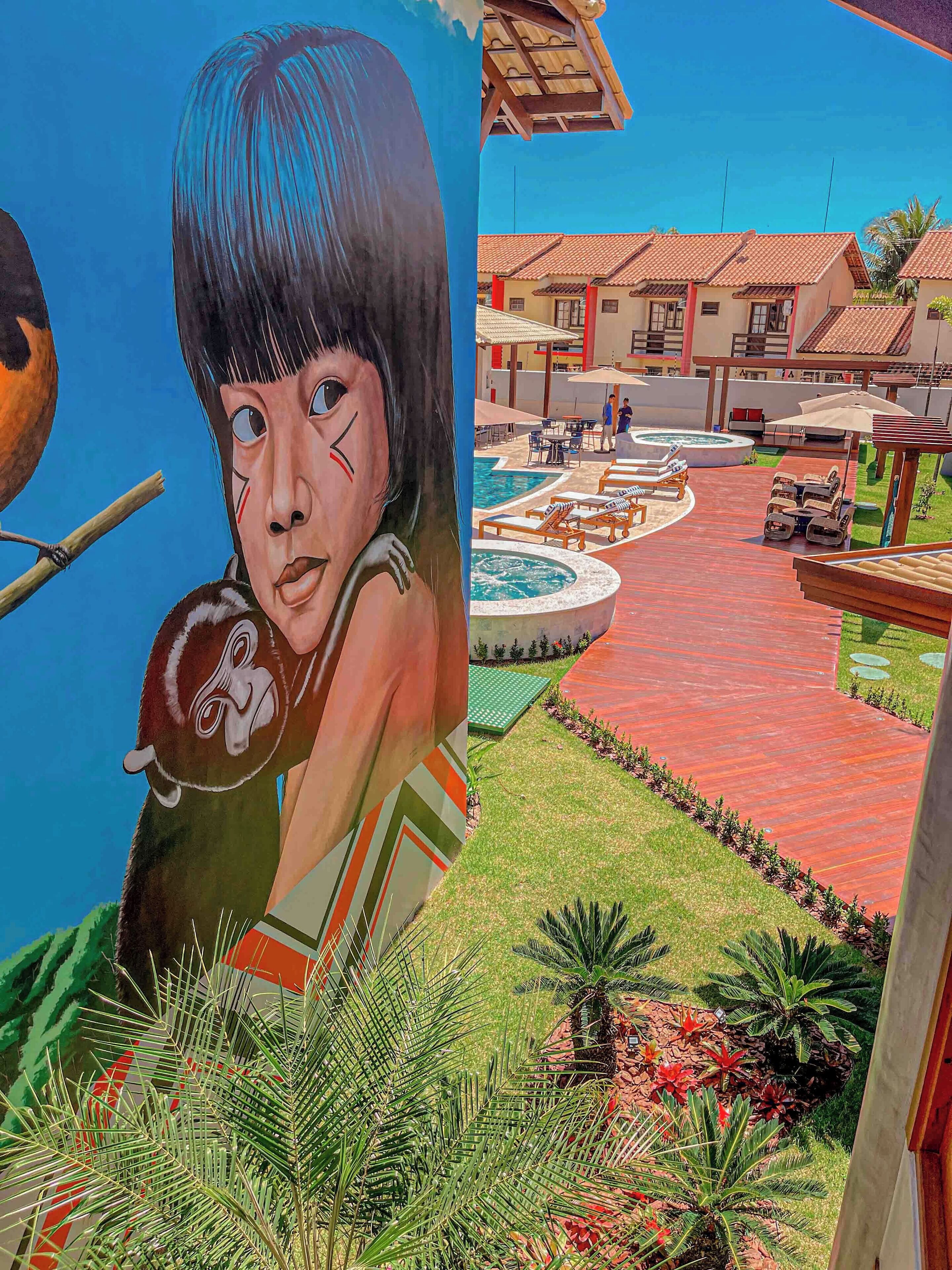 A mural of a child with a bird, a pool area with lounge chairs, and a red-tiled building.