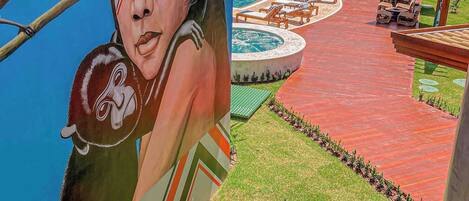 A mural of a child with a bird, a pool area with lounge chairs, and a red-tiled building.