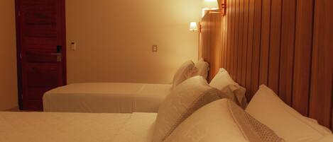 A hotel room with two beds, wooden headboard, and wall-mounted lamps.