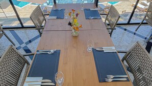 A dining table with a vase of flowers, set for two, overlooking a pool area with lounge chairs and umbrellas. - Príncipe do Muta Hotel Design (Santa Cruz Cabralia)