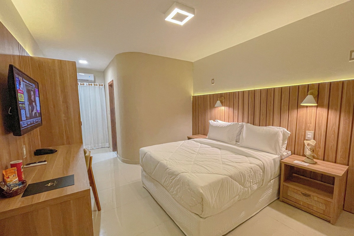 Una habitación de hotel moderna con una cama grande, un cabecero de madera, una mesita de noche con lámpara y un televisor montado en la pared.