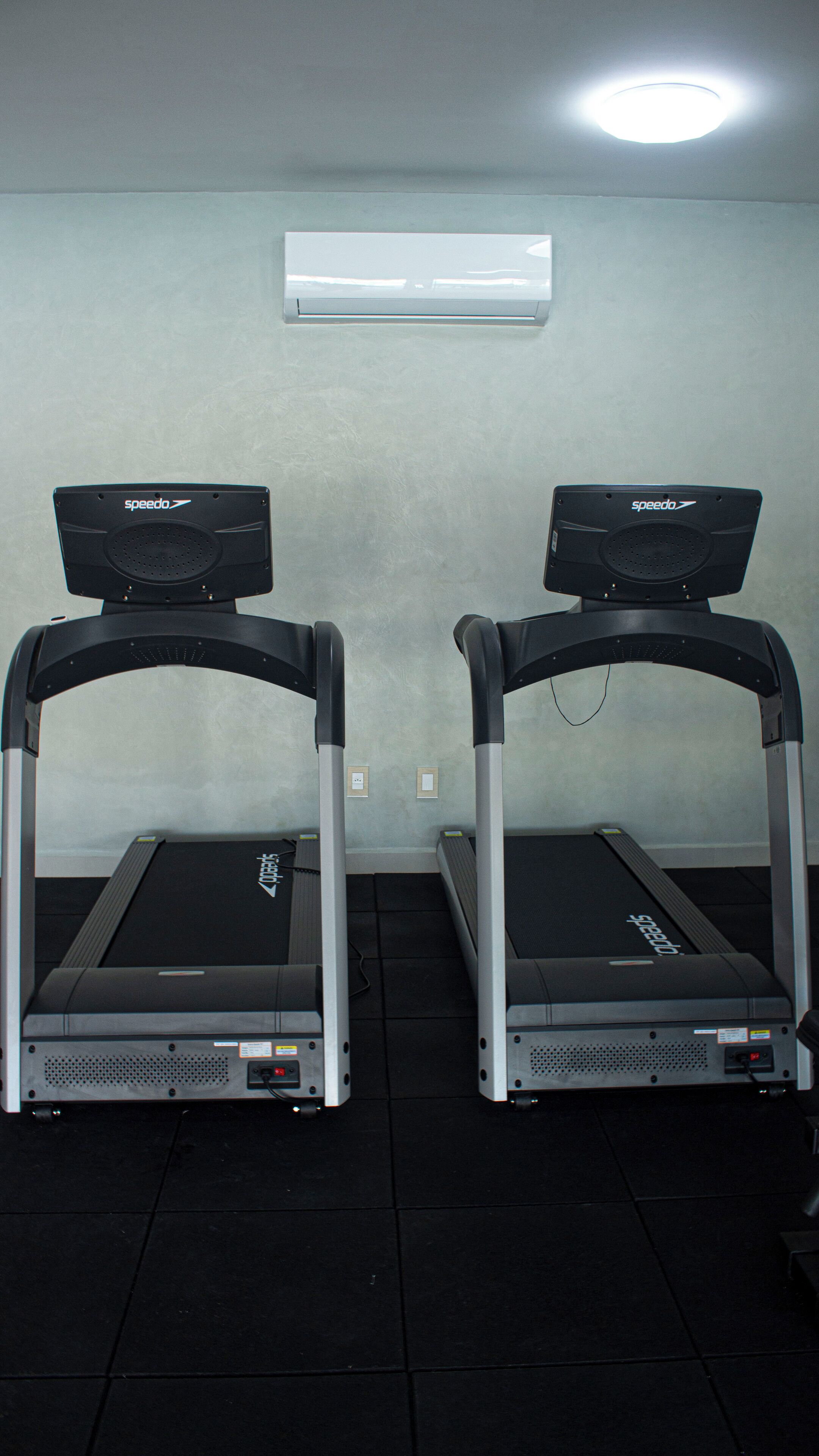 Two treadmills in a room with a plain wall and a ceiling light.