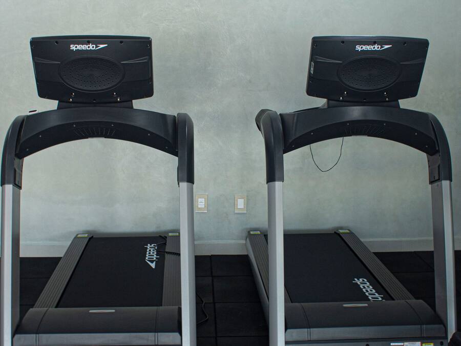 Two treadmills in a room with a plain wall and a ceiling light.