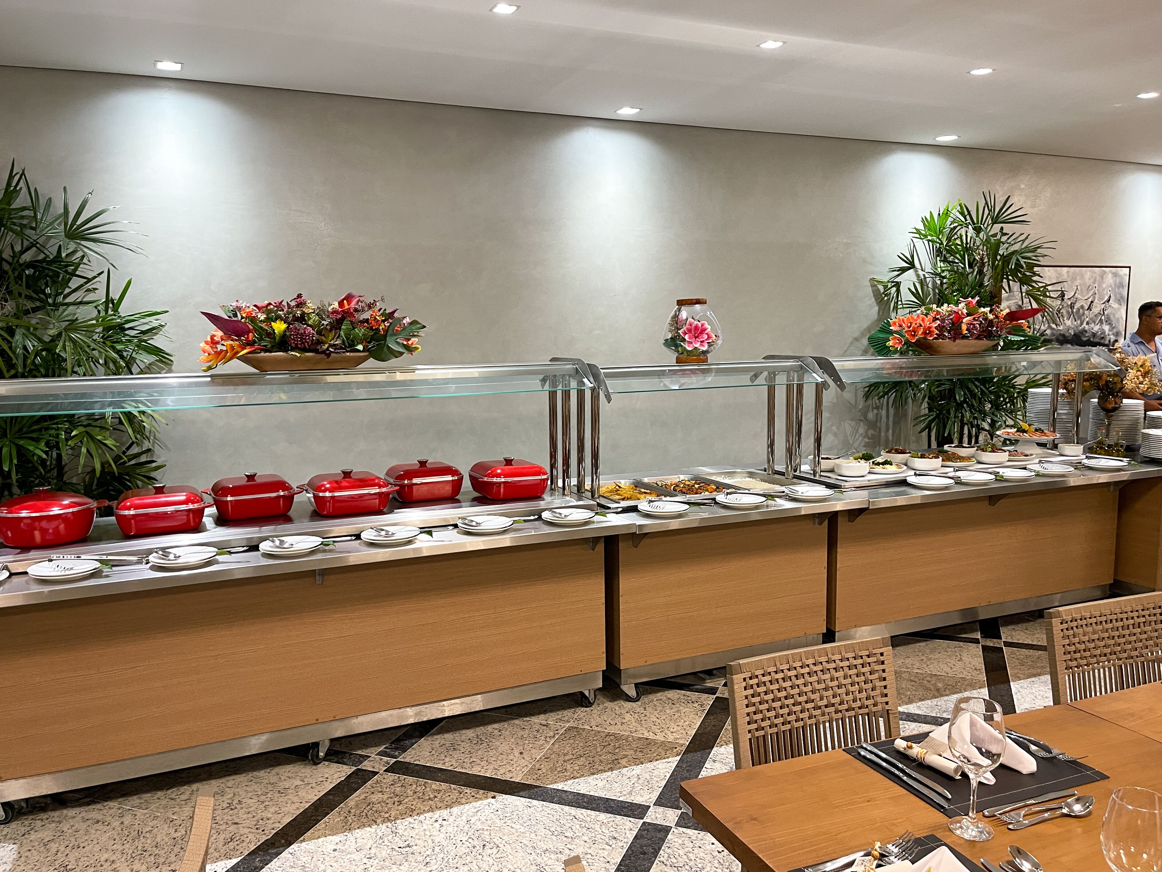 A buffet area with a variety of food items, a glass display case, and a seating area with wooden chairs and a table set for dining.