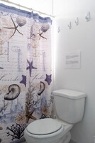 Un baño con cortina de ducha con motivos náuticos, un inodoro blanco y un papel higiénico en la pared.