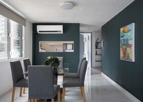 Un comedor moderno con una mesa de vidrio, sillas tapizadas en gris y una planta en maceta.