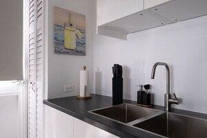 Una cocina moderna con un lavamanos doble, un cuadro de un tarro en la pared y un bloque de cuchillos negros.