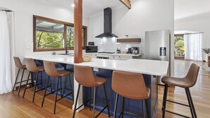 A modern kitchen with a central island, bar stools, a large window, and a view of greenery. - Sublime Mountains Escape: Luxury & Serenity (Leura)