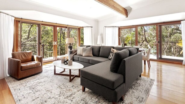 A spacious living room with a sectional sofa, a coffee table, and a leather armchair. Large windows offer a view of the outdoors. - Sublime Mountains Escape: Luxury & Serenity (Leura)