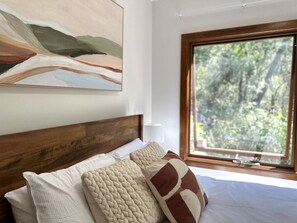 A bedroom with a wooden headboard, a large window with a view of trees, and a painting on the wall.