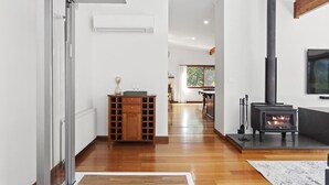 A modern interior with a wood-burning stove, a glass door leading to a balcony, and a kitchen area in the background. - Sublime Mountains Escape: Luxury & Serenity (Leura)