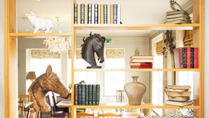 Uma biblioteca com estantes, uma escultura de cavalo e um vaso.