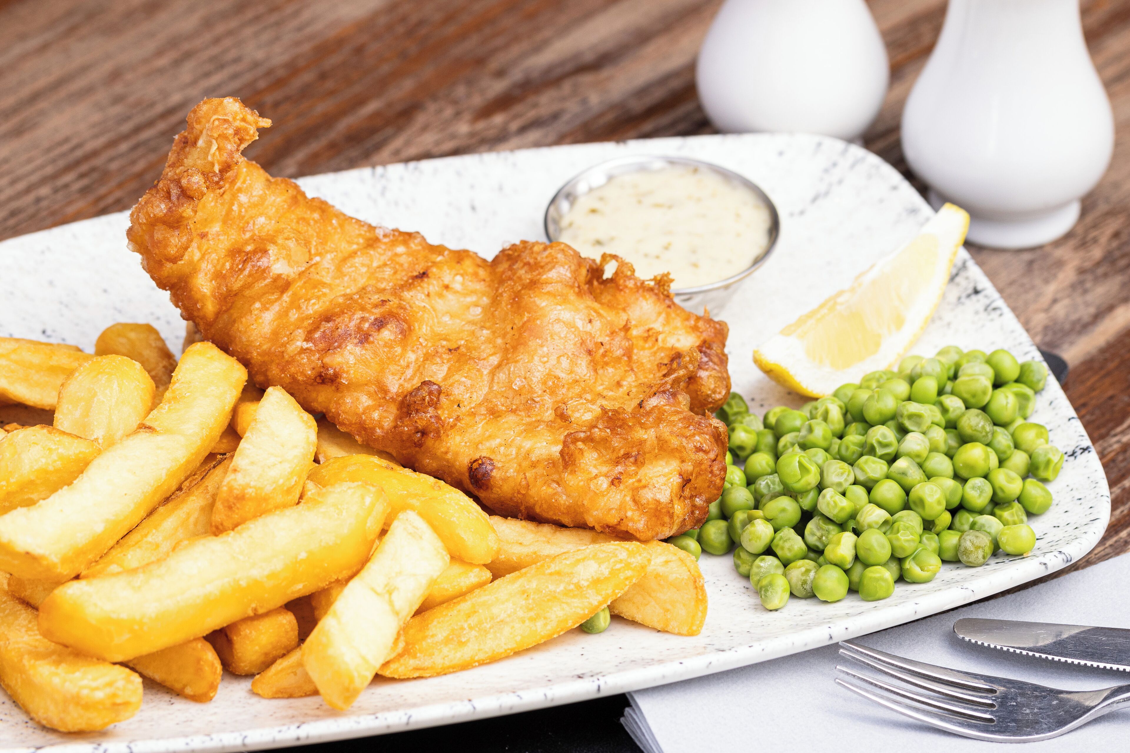 A plate of fish and chips with peas and a lemon wedge.