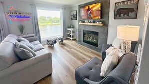 Una sala de estar moderna con un amplio ventanal, chimenea, televisor y ventilador de techo.