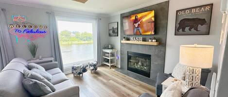 Una sala de estar moderna con un amplio ventanal, chimenea, televisor y ventilador de techo.