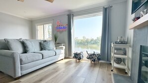 Una sala de estar moderna con un sofá gris, piso de madera, una chimenea y vistas a un lago.