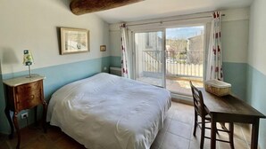 A bedroom with a bed, a desk, and a chair. There is a window with curtains and a balcony visible. - Village house “Stella” (Saint-Cannat)