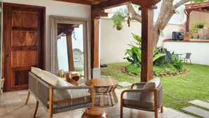 Un patio exterior con muebles de madera, un jarrón decorativo y vistas al jardín.