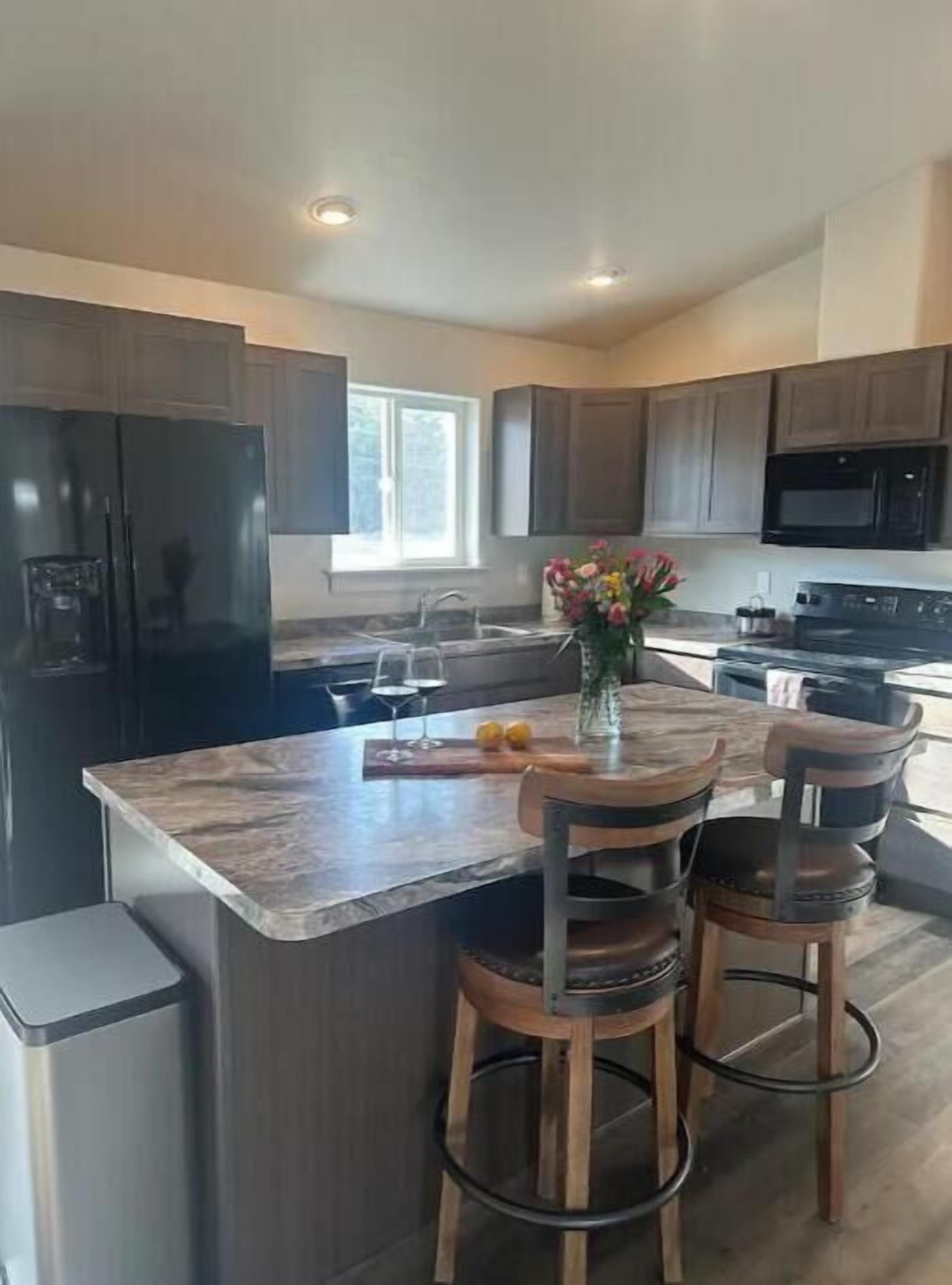 Una cocina moderna con una isla central, taburetes de bar, un refrigerador y un microondas.