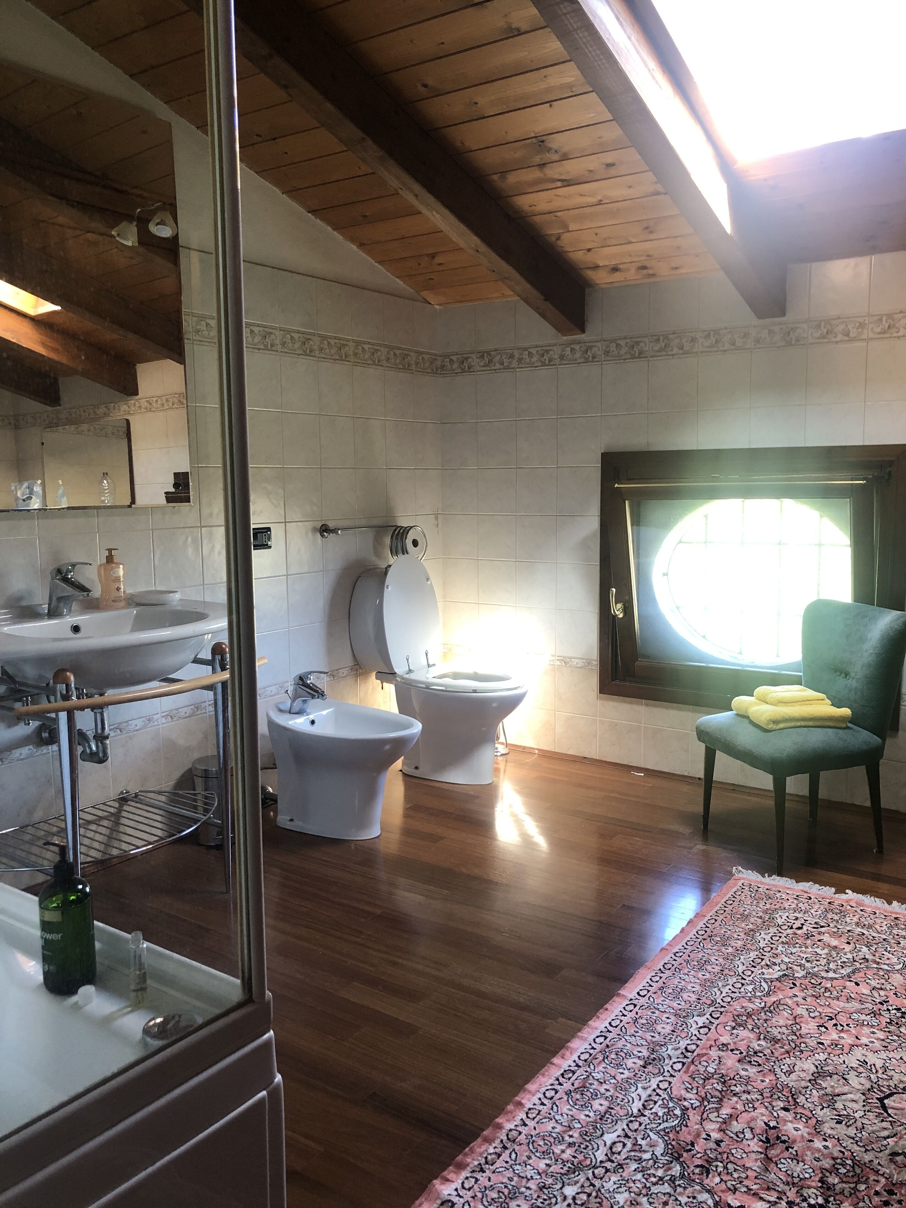 Casa de banho com lavatório, bidé, sanita e uma cadeira.