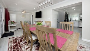 Un espace repas moderne avec une table et des chaises en bois, un ventilateur de plafond et un téléviseur à écran plat fixé au mur.
