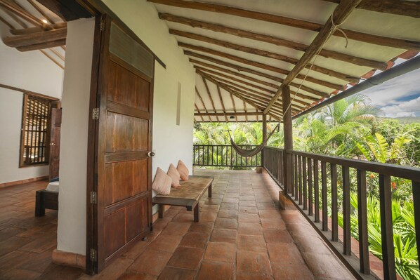 A covered porch with a wooden bench, a hammock, and a view of lush greenery. - Achiotte by Masaya Collection (Barichara)