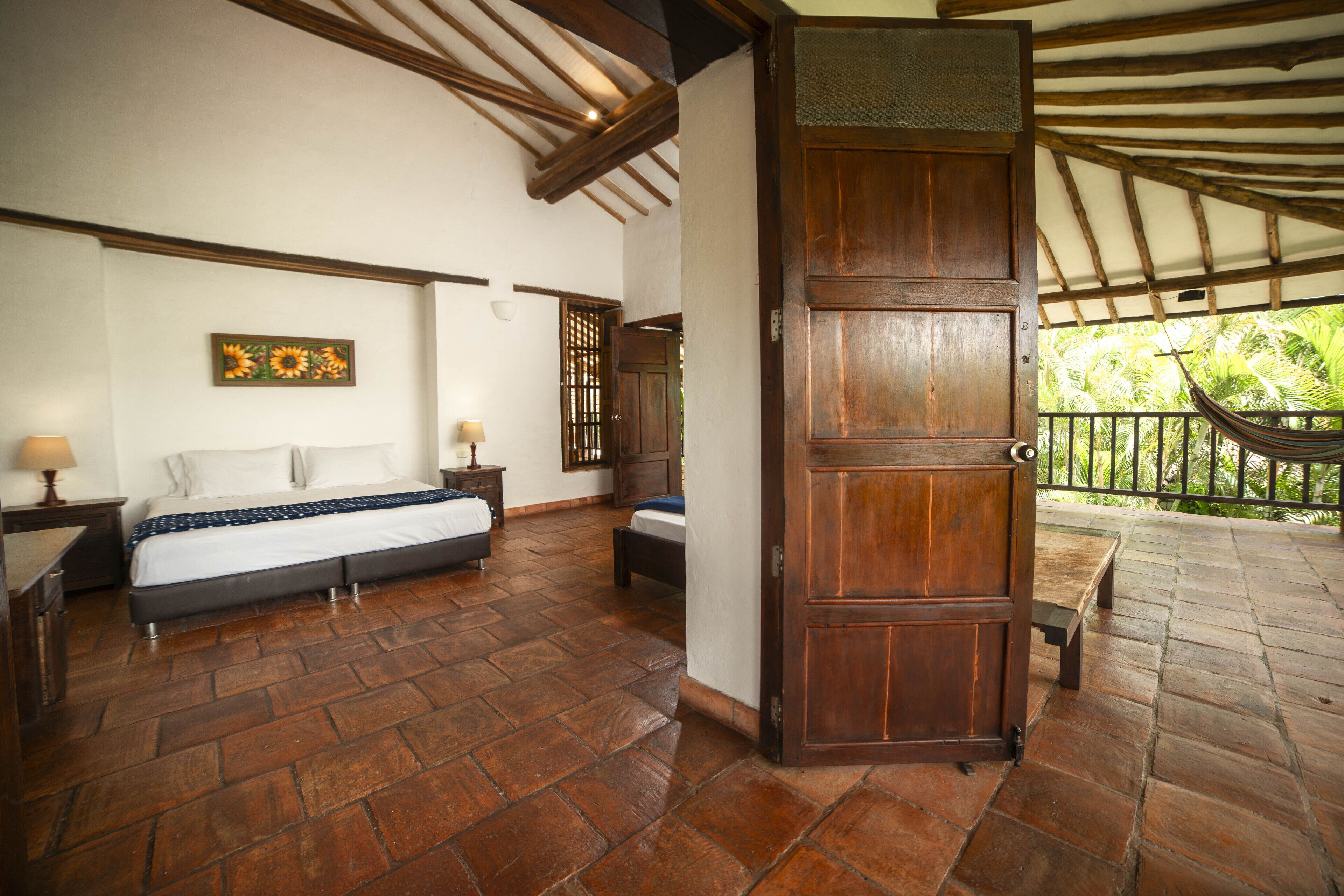 A bedroom with a large bed, a wooden wardrobe, and a balcony with a hammock.